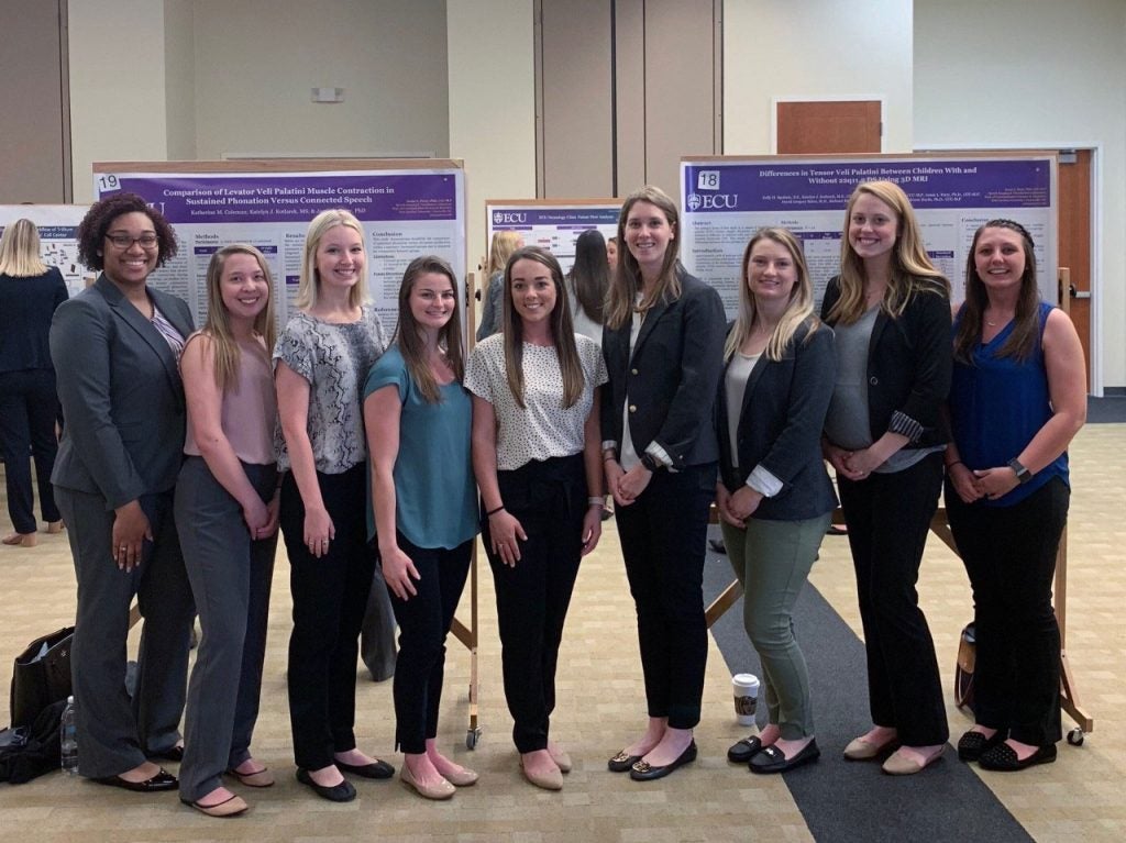 Group of nine female students at a research poster presentation.